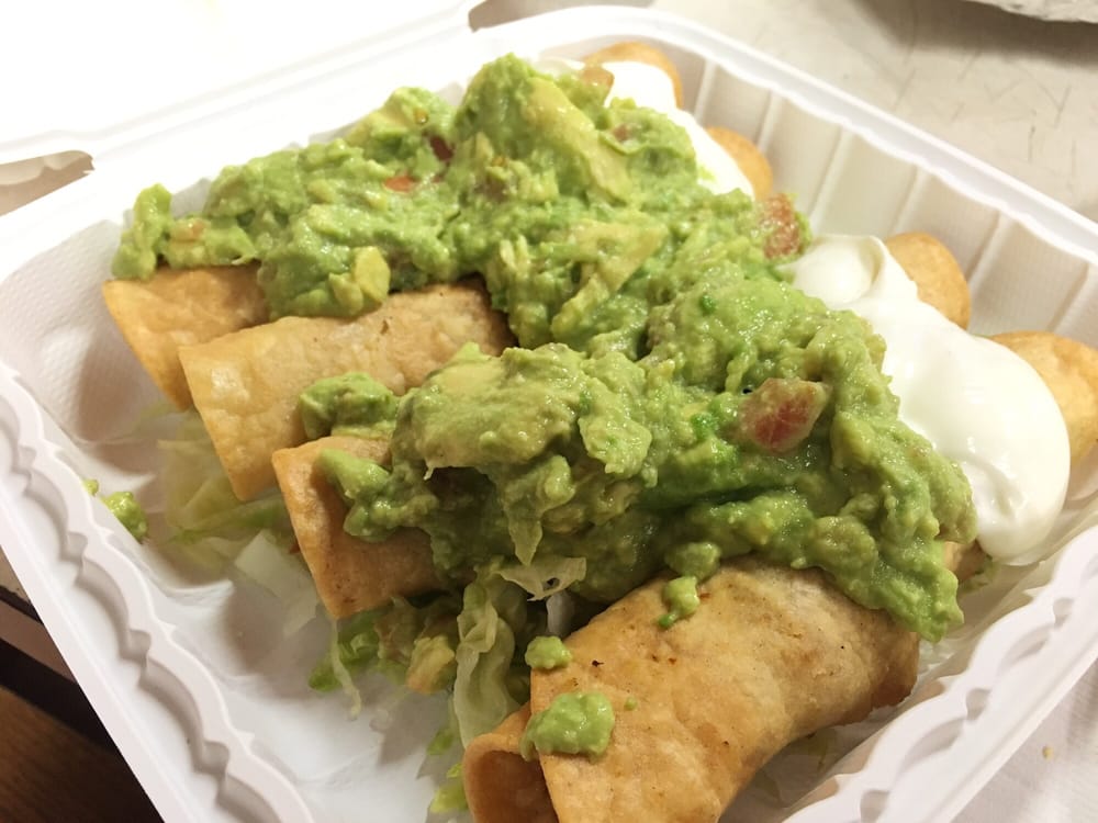 Flautas topped with generous guacamole and sour cream in a takeout container