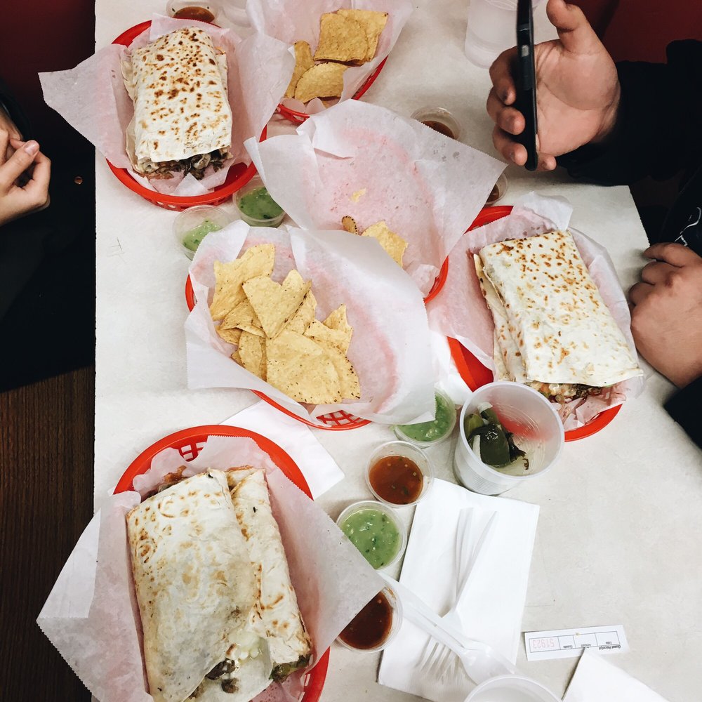 Table spread of super burritos, chips, and salsa cups with green, red, and pico de gallo